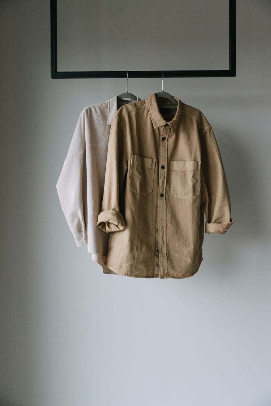 Camisas en tonos neutros colgadas contra una pared blanca