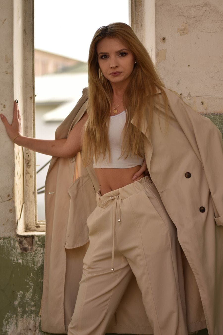 Modelo con trench beige y pantalón amplio junto a una ventana