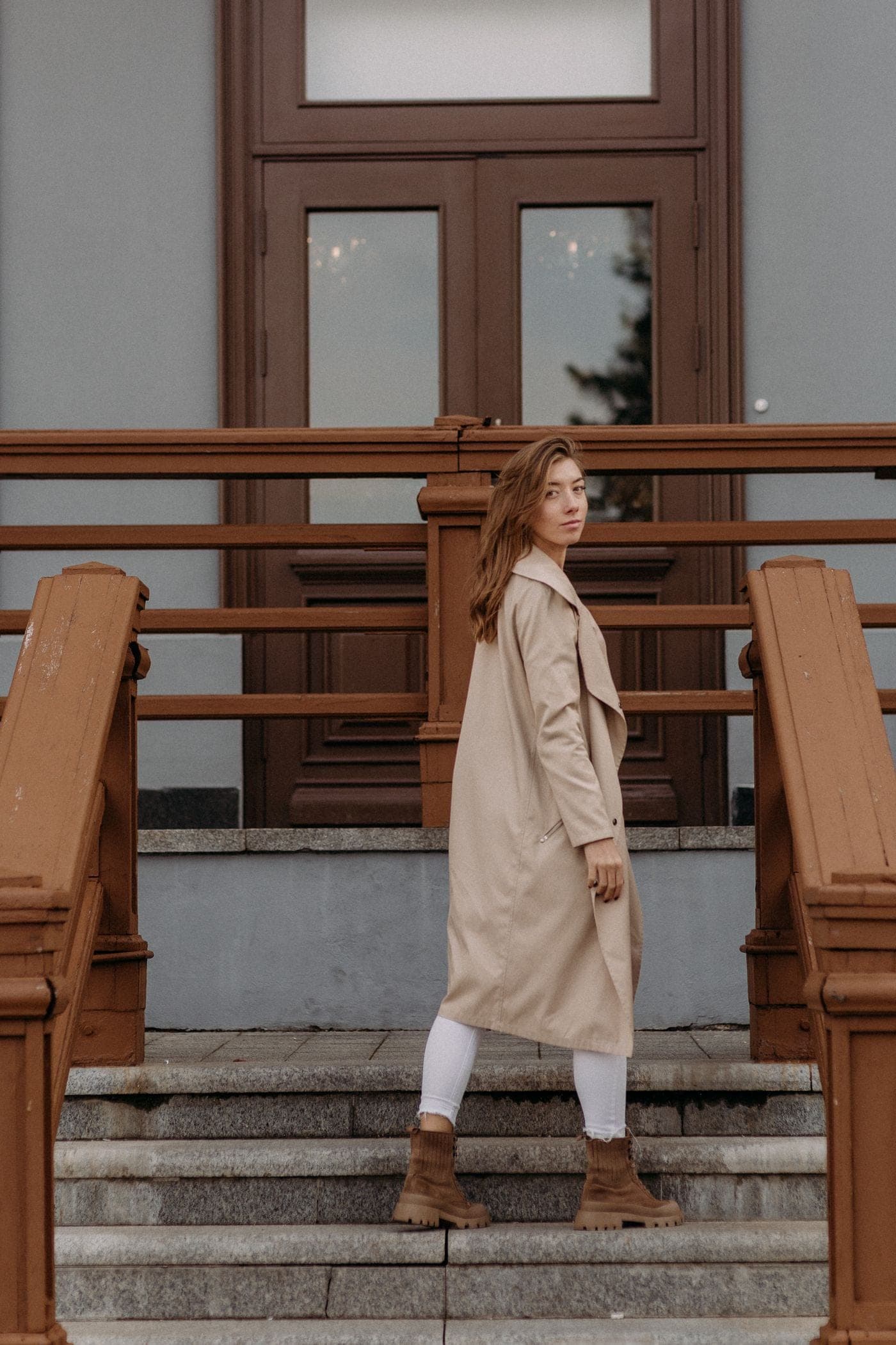 Modelo con trench de algodón color piedra en una escalera de madera